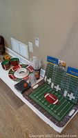 Wide view of the four plastic football platters including three round and one rectangular, cups, napkins, straws, and packaged tailgate trays.