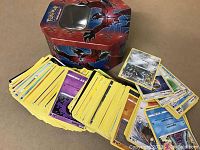Photo of over 200 Pokémon trading cards fanned out next to a collectible metal tin with Pokémon artwork.