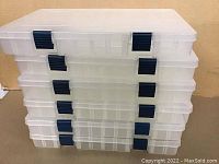 Stacked view of six clear plastic Plano storage cases with dark blue latches.