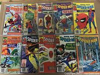 Photo showing 12 vintage Spider-Man comic books arranged on a floor in mostly high-grade condition within plastic sleeves.