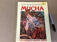 Front cover of the softcover art book titled 'Alphonse Mucha: The Complete Graphic Works' with vintage graphic art design.