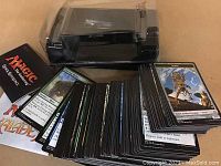 Photo showing a black Magic the Gathering Card Reference box, a spread of approximately 85 Magic the Gathering cards, and a clear plastic card holder.
