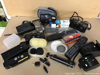 Wide view of the lot showing various camera accessories including lens cases, remote controls, camera light meter, and a boxed projection lamp.