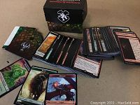 Deck of Magic: The Gathering cards spread and stacked next to a card box and playmat with scaled pattern and Magic: The Gathering logo