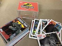 Photo showing the Jurassic Park card box, full deck of cards, and a fan spread of various sticker cards included in the set.