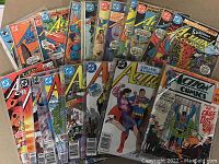 Photo of 25 vintage Superman Action Comics arranged on surface, many in plastic protective sleeves, showing different cover artworks and varying conditions from high grade to used.
