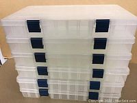 Stack of six clear plastic Plano storage cases with black locking clasps, showing the exterior of the cases.