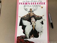 Cover of book titled '100 Years of Posters of the Follies Bergere and Music Halls of Paris' featuring an illustrated performer with swans and stylized text.