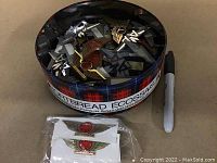 Photo of a tartan patterned metal Port Bread Écossais tin filled with numerous vintage metal airline pins, including large winged Air Canada pins.