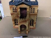 Full front view showing the exterior of the Wayne Manor playset with tan walls, castle-style grey roof, and an arched doorway.