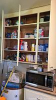 View of wooden cabinets filled with household containers, cleaning supplies, light bulbs, and small appliances above a microwave and water heater.