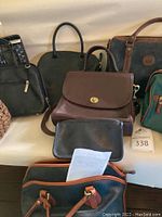 Photo showing a collection of handbags with various colors including brown, black, and blue suede, laid on a white surface