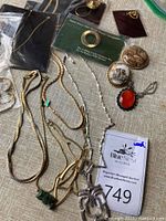 Various costume jewelry pieces including necklaces, pendants, pins, and a ring arranged on beige fabric background.