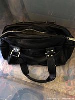 Overhead view of a black leather handbag with double handles and zipper on top
