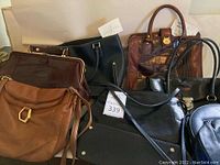 Overview photo showing six assorted leather handbags in various colors and styles, arranged hanging or stacked on a surface.