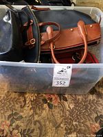 Photo of assorted leather handbags inside a plastic bin showing brown and black bags with handles and zipper closures.