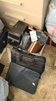Photo showing a black laptop carrying case along with a box containing multiple camera cases and carrying items, including a brown leather case.
