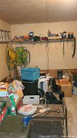 Wide view of garage with storage bins, lawn chairs, yellow extension cords, and other miscellaneous items on shelves and floor.