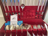 Photo of the complete flatware set in wooden case with red velveteen lining showing various pieces of cutlery including forks and spoons organized in slots.