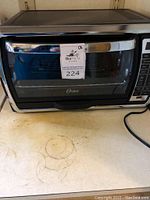 Oster convection oven front view showing glass door with metal handle, visible wire rack inside and oven on kitchen counter