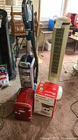 Wide shot showing Shark vacuum, tower heater, Honeywell heater box, and red Sunbeam mini fridge on carpet.