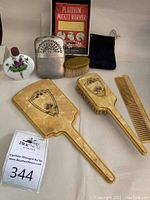 Full assortment of hand mirror, hairbrush, comb, small brush, platinum pocket warmer in box, small floral bottle, and black pouch.