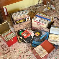 Two cardboard boxes of assorted vinyl LPs and a pile of 45 RPM singles in sleeves on floor