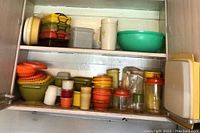 Full view inside cabinet showing assorted vintage Tupperware plastic containers including bowls, measuring cups, and stackable storage containers in various colors