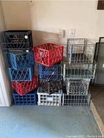 Stacked assorted colored plastic milk crates including blue, red, black, white and grey in a garage corner.