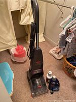 Upright Bissell vacuum cleaner standing on carpet next to two Bissell cleaning solution bottles.