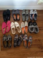 All 12 pairs of Bobs and Toms shoes arranged in rows on a wooden floor, showing a variety of colors, patterns, and designs.