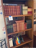 Four-shelf oak bookshelf with assorted classic volumes on top three shelves and modern paperbacks on bottom shelf