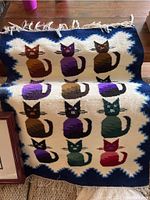 Woven rug featuring twelve cartoon-style cats in rows surrounded by a white and blue zigzag border with fringe on edges