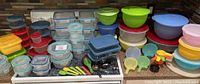 Wide view of all plastic and glass food storage containers, measuring spoons and cups on a stove and countertop.
