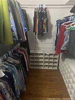 Overview of three hanging rods filled with tops and jackets plus two white cube storage units on floor