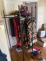 Angle showing the full metal clothing rack loaded with quilts and textiles, demonstrating hanging bars and shelves.