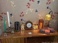 Full display of all lot items on a wooden surface showing candleholders, stained glass pieces, decorative houses, clock, nesting boxes, and lamp.