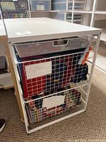 Shot of white Elfa shelving unit full of fabric in wire mesh baskets showing large pieces labeled flannel in the middle basket and smaller fabric pieces below. Top shelf contains sewing notions.