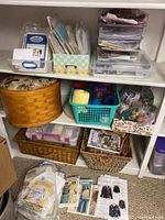 Overview of shelving unit with baskets and containers holding embroidery supplies including patterns and floss.