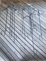 Photo of eleven metal garden hangers arranged on wooden decking showing varying hook designs, heights and styles.