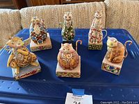 Photo of six colorful Jim Shore cat figurines displayed on blue surface.