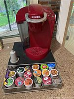 Front angle view of the red Keurig coffee maker, pod drawer, and assorted coffee pods