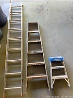 Photo showing three different ladders laid on concrete floor: very long 26-foot extension ladder, medium 16-foot extension ladder folding to 8 feet, and short 6-foot step ladder with blue Cosco top.