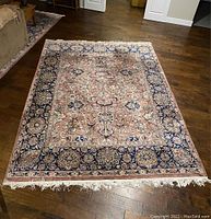Full view of Persian style hand-woven area rug laid on hardwood floor showing detailed floral pattern and fringed edges.
