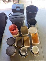 Photo showing a group of nine trash cans and more than twenty plastic pails/buckets of various sizes, shapes and colors.