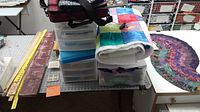 Overview of quilting supplies on a cutting mat including storage drawers, rulers, fabric, and quilts.