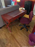 Red desk with three drawers and red upholstered rolling chair next to it, showing desk surface and chair base