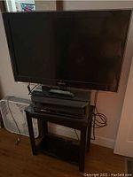 Full view of Samsung TV on black stand with Blu-ray player and fan beside it.