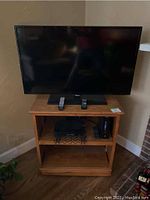 Full view of the Samsung TV on the oak media stand with two remotes placed on the stand.