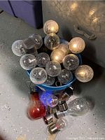 Bucket filled with over a dozen clear and amber crackle globe solar bulb stake lights and several colored decorative hanging solar bulbs in red and blue.